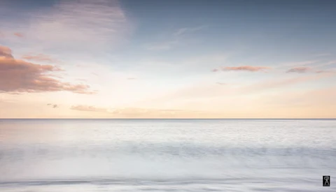 Serene seascape at sunset with soft waves and pastel-colored sky reflecting calm waters.