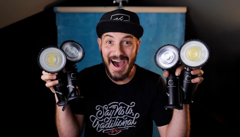 Enthusiastic man holding four LED panel lights in front of a blue backdrop.