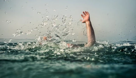 Person struggling in turbulent ocean water with one arm raised above the surface.