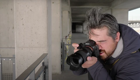 Photographer holding a DSLR camera with telephoto lens while composing a shot in an industrial concrete corridor.