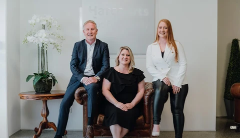 Three professionals posed together in a minimalist studio setting with white walls and decorative plants.