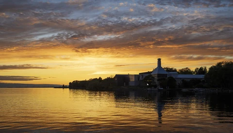 Silhouetted waterfront buildings reflected in calm water at golden hour sunset.