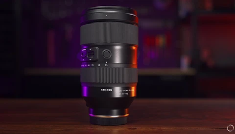 Tamron telephoto zoom lens displayed vertically on wooden surface with purple and orange accent lighting.