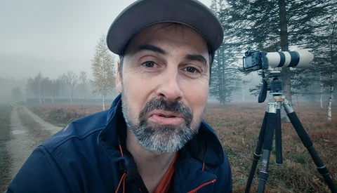 Photographer with telephoto lens on tripod in misty forest landscape.