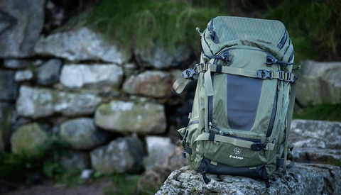 Green hiking backpack sitting on a mossy stone wall with blurred foliage in the background.