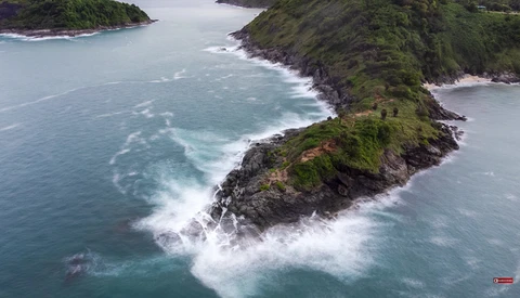 Aerial view of a steep, vegetation-covered peninsula jutting into turquoise ocean with white wave patterns.