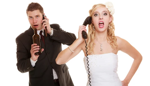 Man in dark suit and woman in white dress holding vintage rotary telephone handsets to their ears with surprised expressions.