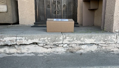 Cardboard delivery box placed on a weathered doorstep with cracked concrete and peeling paint.