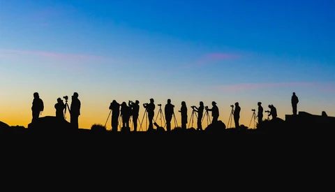 Silhouetted group of people standing on a ridge against a golden and blue sunset sky.