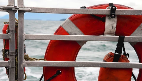 Red and white life preserver rings mounted on gray metal railing with ocean waves visible in background.