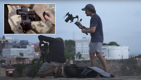 Two videographers operating gimbal stabilizers on a rooftop overlooking an urban skyline at dusk.