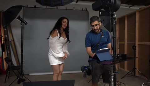 Photographer reviewing footage on tablet while model poses in white dress during studio shoot.