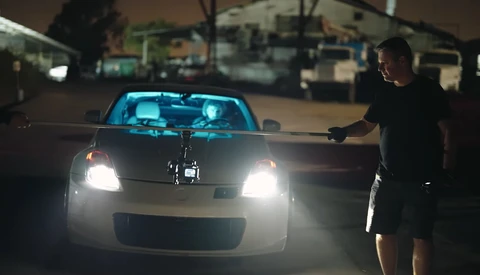 Person in black clothing reaching toward headlights of illuminated white vehicle in covered parking structure at night.
