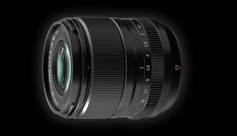 Black camera lens with focus and aperture rings against a dark background.