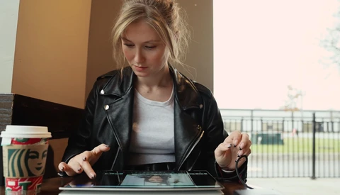 Woman with blonde hair wearing black leather jacket looking down at tablet device.