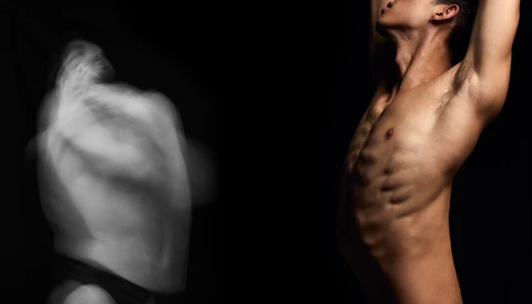 Shirtless male figure with defined abdominal muscles against black background, arm raised above head.