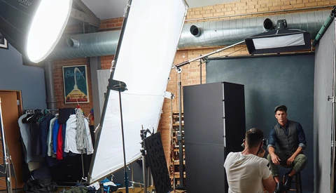 Professional photography studio setup with two people during a portrait shoot, featuring large softbox lighting and reflector panels.