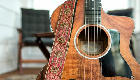 Acoustic guitar with decorative red and gold strap in an interior space with wooden furniture.