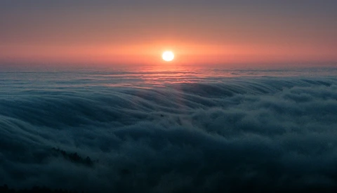 Sunrise over a sea of clouds with the sun glowing orange above the cloud layer.