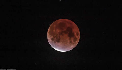 Blood moon during total lunar eclipse with deep red coloration and visible surface details against black sky.