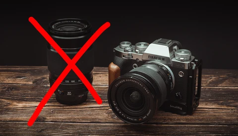 Vintage film camera next to a rejected zoom lens with red X mark on wooden surface.