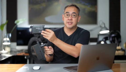 Content creator demonstrates a gimbal stabilizer while seated at a desk with laptop.