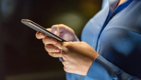 Person in blue shirt holding smartphone with stethoscope visible, shallow depth of field background.