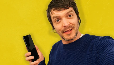 Man holding a black rectangular object against a bright yellow background.