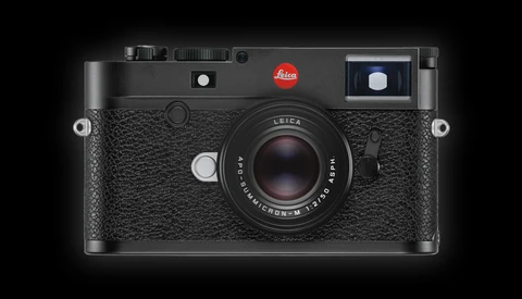 Leica M rangefinder camera with black leather body and 50mm lens against dark background.