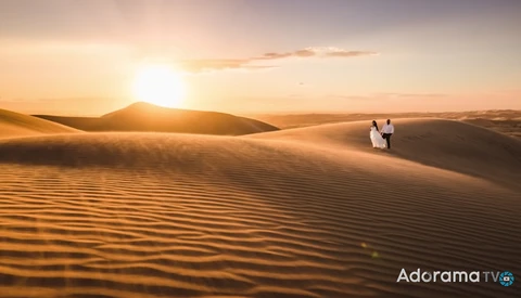 Couple in white clothing standing on a desert sand dune during golden hour sunset.