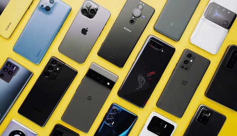 Flat lay of approximately 12 smartphones arranged on a bright yellow background, displaying various models and finishes.