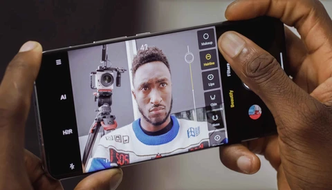 Smartphone camera interface displaying a portrait of a person with a camera mounted on a tripod visible in the mirror reflection.