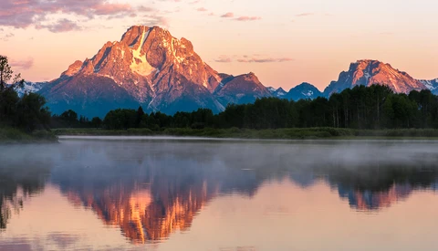 Mountain peak glowing in golden alpenglow light reflected in still water at sunset.
