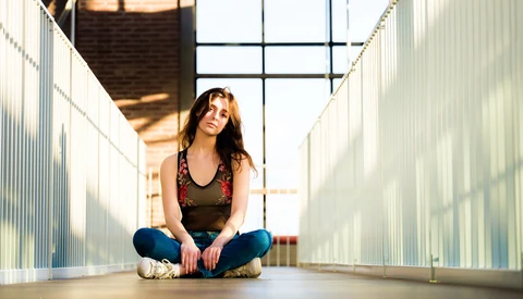 Woman sitting cross-legged in an industrial corridor with metal walls and overhead skylight.