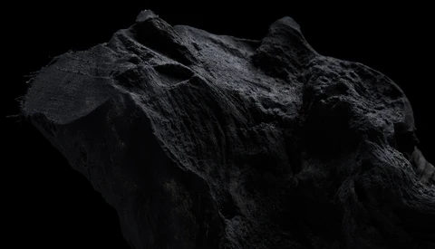 Dramatically lit dark rock formation against black background, showcasing rugged texture and angular peaks.
