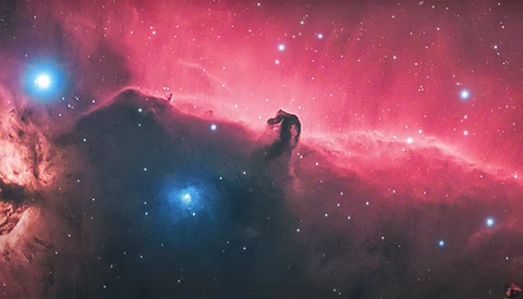 The Horsehead Nebula silhouetted against glowing pink hydrogen gas with bright blue stars scattered throughout the cosmic dust.