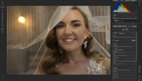 Woman in white lace dress and veil smiling at camera in warm indoor lighting.