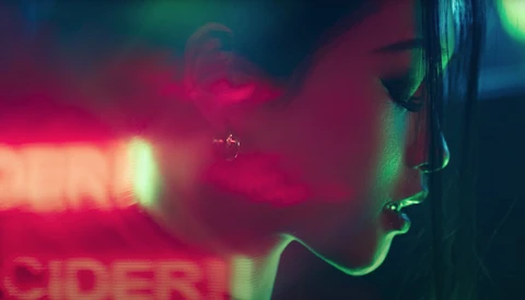 Profile of a person's face illuminated by neon pink and green light against a dark background.