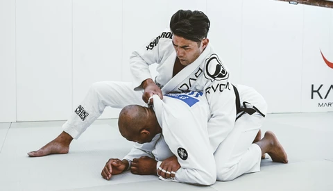 Two martial artists grappling on a white mat during a Brazilian jiu-jitsu training session.