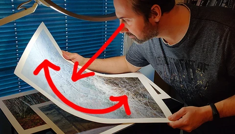 Photographer examining printed photographs with red arrows indicating comparison between prints.