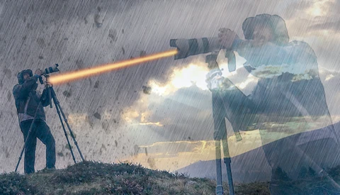Photographer with telephoto lens on tripod firing a beam of light toward a translucent overlay of a businessman and building.