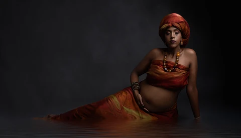 Woman in red-gold costume reclining in shallow water against dark background.