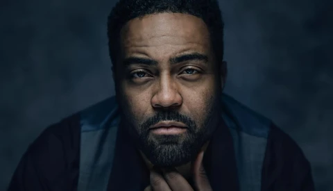Man with beard looking directly at camera against dark blue background.