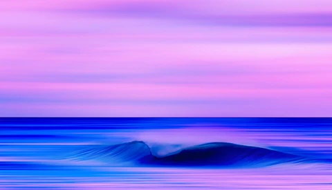 Ocean wave with motion blur against a vibrant pink and purple twilight sky.