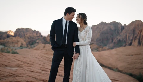 Bride and groom in formal attire standing together in a desert landscape at golden hour.