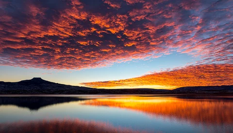Dramatic sunset sky reflected in still lake water with mountain silhouette.