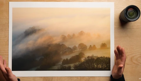 Misty landscape with forested hills bathed in golden morning light beneath overcast skies.