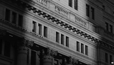 Black and white architectural detail of a classical building facade with ornate Corinthian columns and stone balustrade.