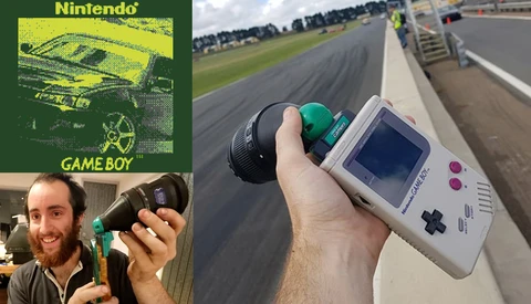Person holding a Game Boy at a racing track with a telephoto lens visible in background.