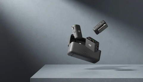 Compact camera charging dock with detached battery and lens cap suspended mid-air above white surface.